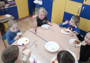 Dzieci siedzą przy stolikach spożywając kanapki zrobione samodzielnie